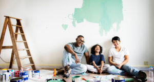 Family of three leaning on a wall laughing together, taking a break from painting one of the rooms of their house